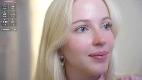 Media: A close-up video of a fair-skinned, blonde woman with light blue eyes, wearing a pink top, looking slightly to the left, with a blurred background.