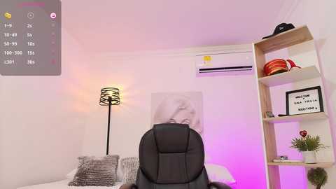 Media: Video of a modern bedroom with a black leather office chair facing a white bed, a wooden bookshelf, a black lamp, and a framed Marilyn Monroe print on the wall.