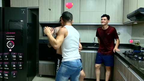 Media: Video of a gym setting with two men; one in a gray tank top and jeans, the other in a maroon shirt and blue shorts, standing by a kitchen counter.