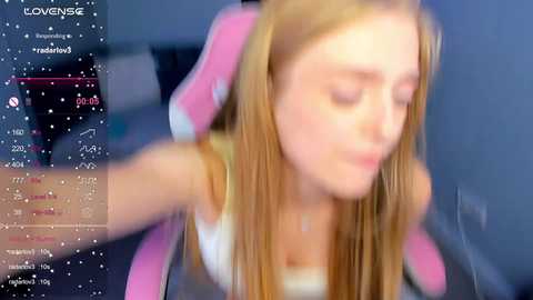 Media: A video of a young woman with long blonde hair and a pink headband, wearing a white tank top, seated in a gaming chair.