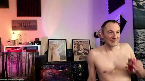 Media: A video of a shirtless man with a short haircut, holding a microphone, in a dimly-lit room with posters, a lamp, and a couch with a sci-fi-themed cover.