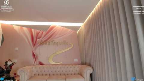 Media: Video of a modern, plush waiting area with a light beige tufted sofa, pink and white floral mural, and vertical, light gray pleated curtains.