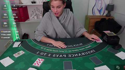 Media: Video of a woman in a grey robe, seated at a green poker table, with playing cards, chips, and a smartphone overlay showing betting information.