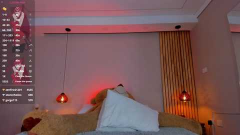 Media: Video of a modern bedroom with a plush brown bed, white pillows, and two red pendant lights. Vertical wooden blinds partially cover a window, casting a warm glow.