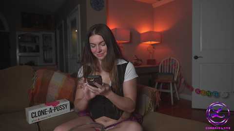 Media: Video of a young woman with long brown hair, wearing a black and white top, sitting on a couch, reading a book titled \"Close-UP.\" The background features a dimly lit room with a colorful rug and a lamp.