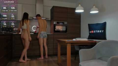 Media: Video of a modern kitchen at night with a man and woman in underwear, checking a smart fridge. Dark wood cabinets, white walls, and a large flat-screen TV.