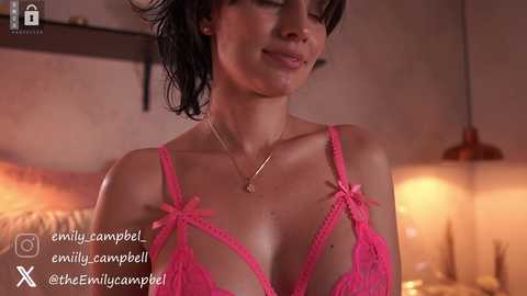 Media: A video of a woman in pink lace lingerie, with a soft smile, in a dimly lit bedroom.