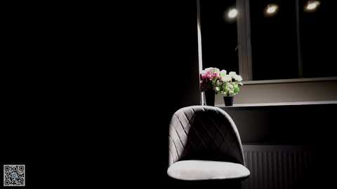 Media: Video of a minimalist interior scene featuring a modern, white chair with a curved backrest, positioned in front of a window with a potted plant of white and pink flowers.