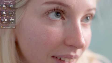 A close-up video of a young woman with fair skin, blue eyes, and blonde hair, smiling slightly, with a weather overlay in the top-left corner.