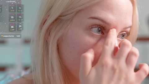 Media: A close-up video of a blonde woman with fair skin, covering her mouth with her hand, with a blurred background showing a calendar.