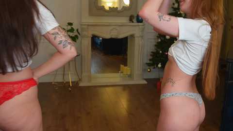 Media: Video of two women in lingerie, one with long red hair and tattoos, dancing in a living room with a Christmas tree.