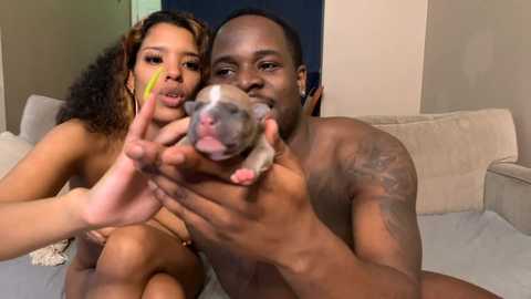 Media: Video of a topless Black man with tattoos and a small puppy in his hands, next to a topless Black woman with curly hair, both smiling.