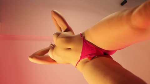 Media: A low-angle video of a light-skinned woman with a slender, toned physique wearing red panties, standing in a room with pink walls. Her arms are raised, accentuating her small breasts.