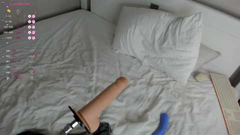 Media: A video of a man with a realistic tan-colored dildo in a white bed with two pillows, a blue vibrator, and a dark-colored headboard.