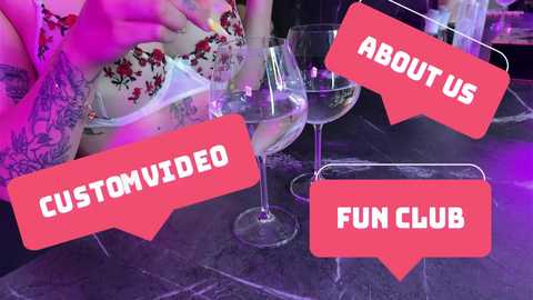 Media: Video of a tattooed woman in a floral dress, holding a wine glass, in a dimly lit, purple-lit club, with \"CUSTOM VIDEO\" and \"FUN CLUB\" red speech bubbles overlaying.