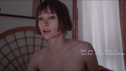 Media: Video of an Asian woman with a short bob haircut, topless, sitting on a chair with a wicker backrest. Background includes beige curtains and wooden furniture. Text overlay: \"See you next time @33 Twitter @TKKOMANSHOW.\