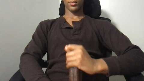 Media: Video of a Black man sitting with a black shirt, holding a wooden cane, against a plain beige wall.