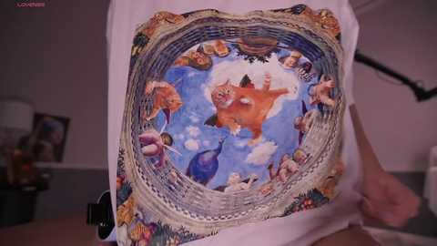 Media: A video of a person holding a white shirt with a colorful, detailed Renaissance painting of a mythical scene, featuring mermaids, sea creatures, and people. The background is a plain, indoor setting.