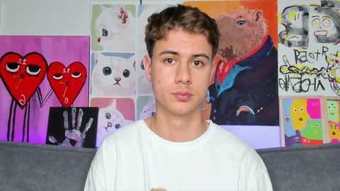 Media: Video of a young white man with short brown hair, wearing a white shirt, standing in front of a colorful wall with various animal and graffiti-themed art.