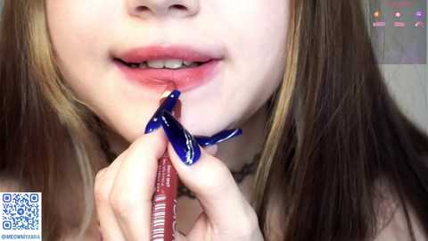 Media: A close-up video of a young woman with light skin and long, straight brown hair, biting into a red and white striped lollipop with blue ribbon.