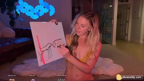 Media: Video of a young, slim, blonde woman in a yellow bra, holding a drawing of a crying face with a red nose, in a modern, dimly lit living room with a plush white rug.