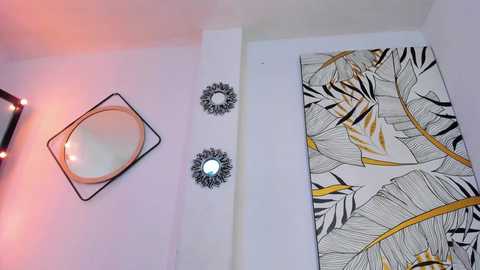 Media: Video of a modern, minimalist bedroom wall featuring a large, abstract banana leaf-patterned tapestry, two circular black and white wall sconces, and a round mirror with a gold frame.