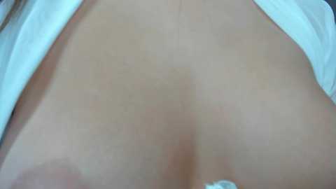 Media: A close-up video of a woman's bare back, featuring a slight tan line and pale skin, with a white garment partially covering the upper portion.