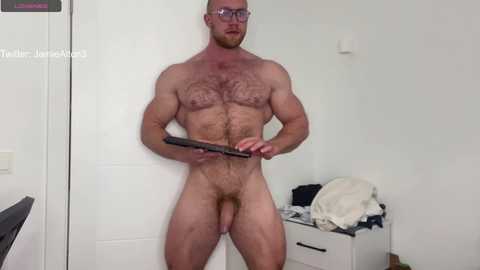 Media: A video of a muscular, bald, bearded, fair-skinned man with glasses, standing naked, holding a black gun, in a minimalist room with white walls and a dresser.