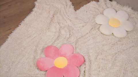 Media: A video showing three soft, plush flower toys with yellow centers, placed on a beige, fluffy rug. Two flowers are pink and one is white.