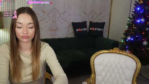 Media: Video of a young woman with long brown hair, wearing a beige sweater, sitting indoors with a Christmas tree in the background.