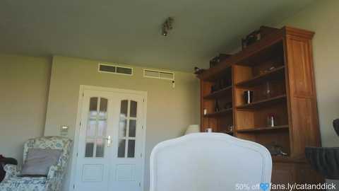 Media: Video of a cozy living room featuring a white armchair, wooden bookshelf, beige walls, and a floral-patterned couch.