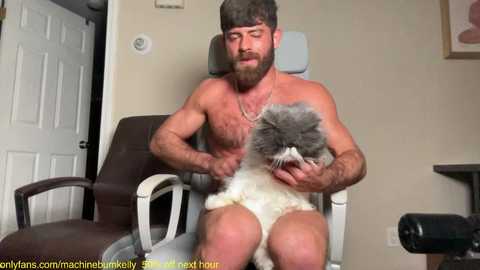 Media: Video of a shirtless, muscular man with a beard and grey beard, wearing a grey beanie, petting a white and grey cat on his lap in a beige room with a closed white door.