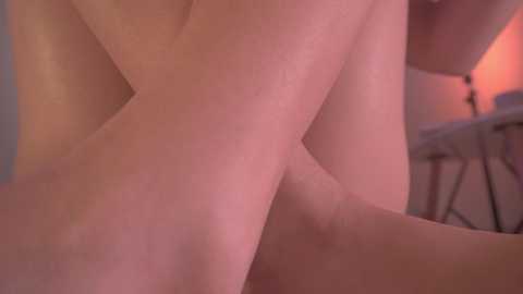 Media: Video of a close-up, partially blurred view of a person's lower torso and legs, with soft, warm lighting creating a sensual ambiance. The background includes a hint of a white table and a lamp with a red lampshade, adding to the intimate setting.