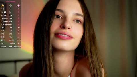 Media: Video of a smiling young woman with long brown hair, fair skin, wearing a pink top, indoors with a blurred, colorful background, displaying a digital screen with a weather app.