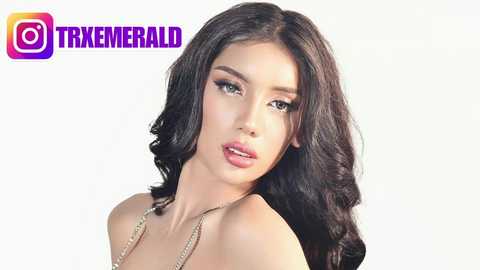 Media: Video of a young woman with long, wavy dark hair, fair skin, and full lips, wearing a gold necklace, set against a plain white background. \"TRIXEMERIAL\" logo in the top left corner.