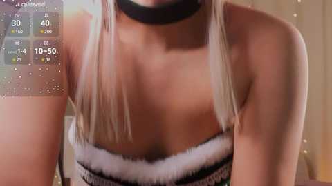 Media: Video of a woman with light skin, wearing a black choker and white fur-trimmed strapless top, showcasing her cleavage. Background shows a digital screen with fitness stats and a blurred, warm-toned indoor setting.