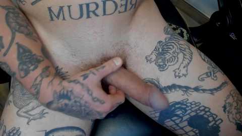 Media: Video of a person with pale skin, tattoos of a tiger, snake, and \"MURDER\" across the torso, and a circumcised penis in hand, sitting on a black chair.