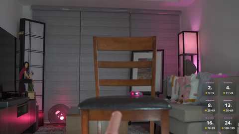 Media: A video of a modern living room with a wooden chair in the foreground, under a dim purple light. The background features a gray sectional sofa, a black folding screen, and a plant.