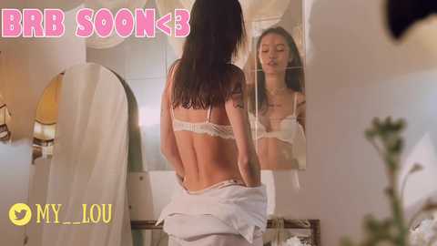 Media: Video of a woman with long dark hair, topless in white lace bra, viewed from behind, in a dimly lit bedroom with mirror. Text overlay reads \"BBB SOOK3\" and \"MYL-IOU.\