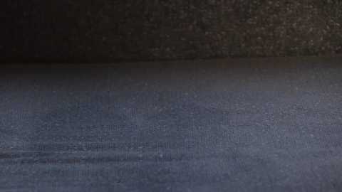 Media: A video of a close-up, dark gray fabric surface with a slightly textured, woven pattern. The fabric appears smooth and uniform, with a slight gradient effect in the lighting. The background is dark, creating a stark contrast.