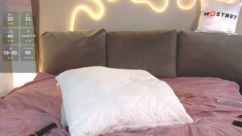 Media: Video of a messy bed with a white pillow, pink sheets, a phone, and a remote control. Neon lights in the background add a modern touch.