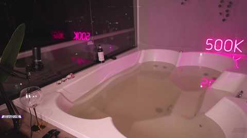 Media: Video of a modern, pink-lit bathroom with a white, oval tub filled with murky water. The tub is adjacent to a large window showing city lights, with a \"500K\" sign glowing in the background.