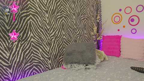 Media: A video of a cozy bedroom with zebra-patterned wallpaper, a gray throw blanket, and a bed adorned with pink pillows and a white duvet. The room features playful, colorful circular stickers on the wall.