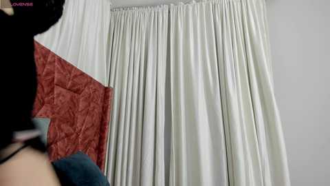 Media: A video of a woman in a white dress with a red patterned sleeve, standing in front of a white curtain with a subtle floral pattern.