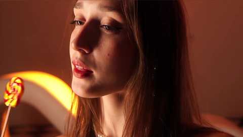 Media: Video of a young Caucasian woman with fair skin, brown hair, and red lipstick, gazing thoughtfully. Warm lighting casts a golden glow, creating a cozy atmosphere.