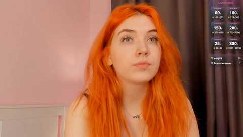 Media: Video of a young woman with long, vibrant orange hair, pale skin, and blue eyes, wearing a white top, against a pink and white wall, with a digital display showing viewer statistics.