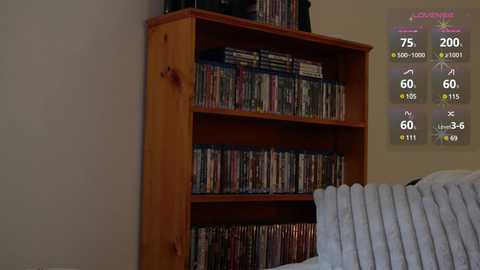 Media: Video of a wooden media cabinet filled with DVDs, positioned against a beige wall. A white bed with a quilted blanket is partially visible in the foreground. A digital clock displaying 7:05 AM and weather forecast is mounted on the wall.