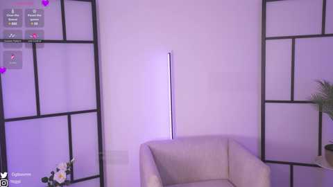 A video of a modern living room with a beige couch, purple-shaded lighting, and black-framed dividers. A tall, sleek floor lamp stands centrally, and a potted plant sits to the right.