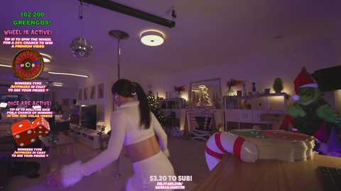 Media: A video captures a woman in a white crop top and high-waisted shorts dancing energetically in a dimly lit, festive living room adorned with Christmas decorations.