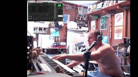 Media: Video of a shirtless, middle-aged, white man with headphones, playing a keyboard in a cluttered, brightly lit recording studio. He's focused on the digital audio workstation screen.